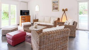 Ein Wohnzimmer mit Rattanmöbeln, einem roten Hocker, einem Fernseher und einem Gemälde an der Wand.