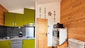 Ett kompakt kök med gröna skåp, diskmaskin, mikrovågsugn och ugn.