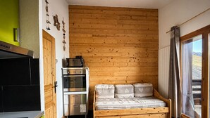 Ett kompakt rum med ett litet kök, en väggpanel av trä, en soffa med kuddar och ett stort fönster med utsikt.