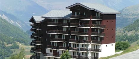 Un hotel de varios pisos con balcones, con montañas al fondo.