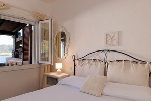 Ein Schlafzimmer mit einem Bett, einem Nachttisch mit Lampe, einem Fenster mit Rollläden, einem Spiegel und einer Wanddekoration.