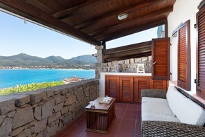 A balcony with a stone wall, wooden furniture, and a view of the sea and mountains. - Casa Matilde con Patio by Wonderful Italy (Olbia)