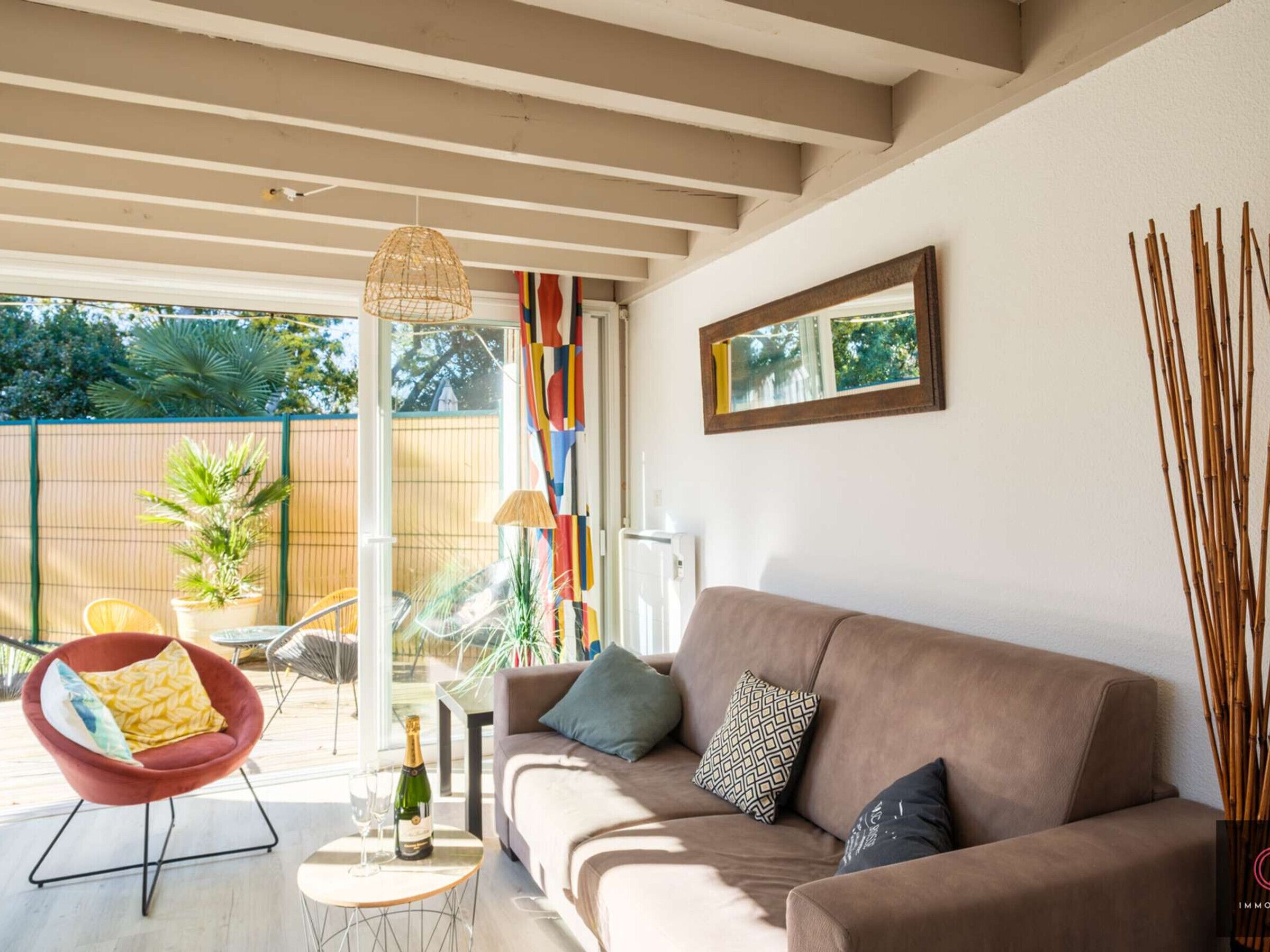 A modern living room with a sofa, a red chair, a table with a bottle and glasses, and a large window.