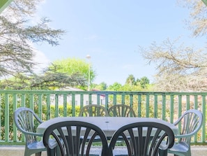 Eine Terrasse im Freien mit Tisch und Stühlen, umgeben von einem grünen Zaun und Bäumen.