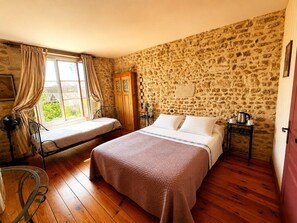 Ein Schlafzimmer mit Steinwand, einem Bett, einem Fenster mit Vorhängen, Holzboden und einem kleinen Tisch mit Wasserkocher.