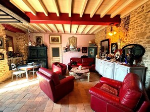 Ein Zimmer mit Steinwand, Holzbalkendecke, einem roten Sofa, einem weißen Schrank und einem Esstisch mit Stühlen.