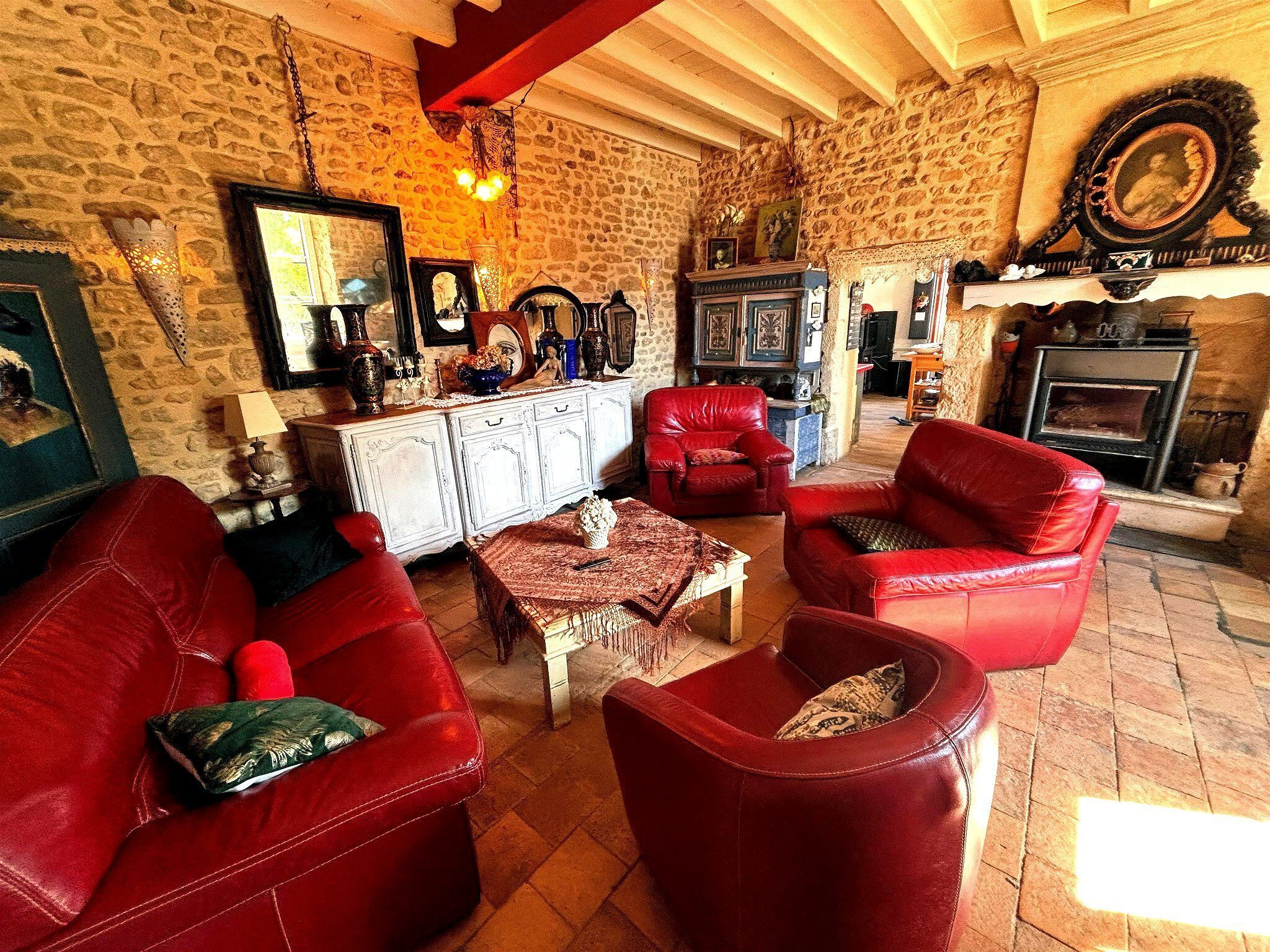 A cozy living room with red leather sofas, a fireplace, stone walls, and a wooden ceiling.