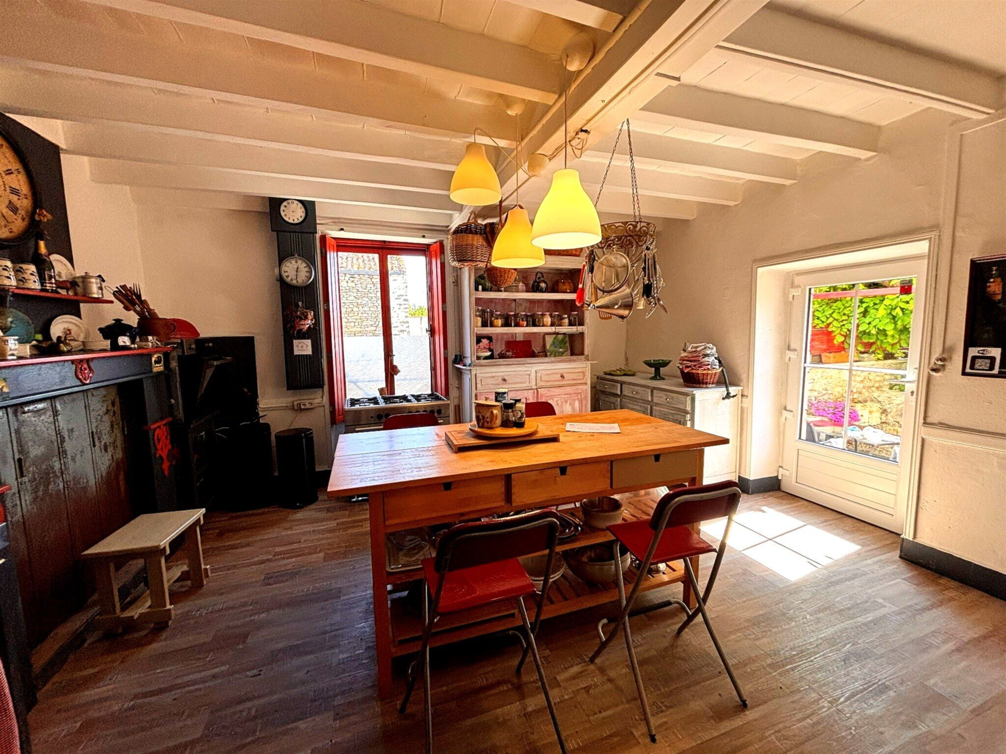 Une cuisine avec une table en bois, des chaises, des lampes jaunes suspendues et une porte rouge.