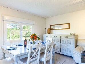 Ein Essbereich mit Tisch für vier Personen, einem weißen Schrank mit Schubladen und einem Fenster mit Blick auf Grünflächen.