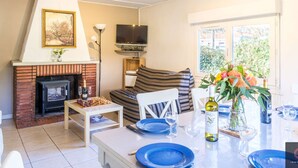 A living room with a fireplace, a television, a sofa, and a dining area with blue plates and wine glasses. - Charming house with parking - 6 guests. Near lake (Biscarrosse)