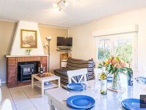 Ein Wohnzimmer mit Kamin, Fernseher, einer Couch und einem Essbereich mit blauen Tellern und Weingläsern.