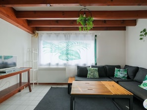 Ein Wohnzimmer mit Sofa, Couchtisch, Fernseher und einem Fenster mit Vorhängen.