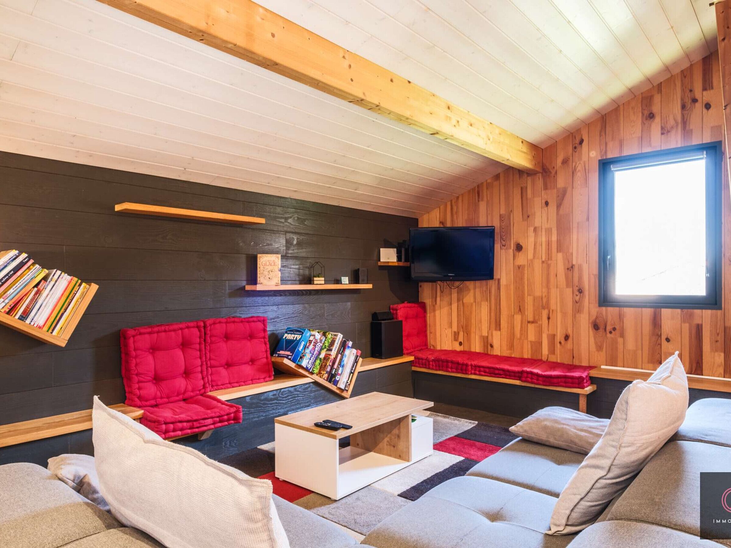A cozy living room with a red sofa, a grey couch, and a TV mounted on the wall.