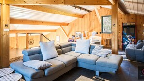 A cozy log cabin interior with a sectional sofa, wooden beams, and a gaming arcade.