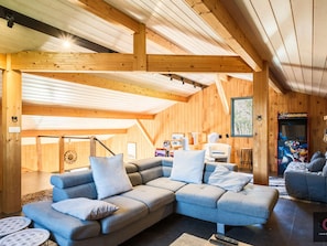 A cozy log cabin interior with a sectional sofa, wooden beams, and a gaming arcade.