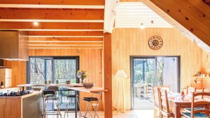 A wooden interior with a dining area, kitchen, and large windows.