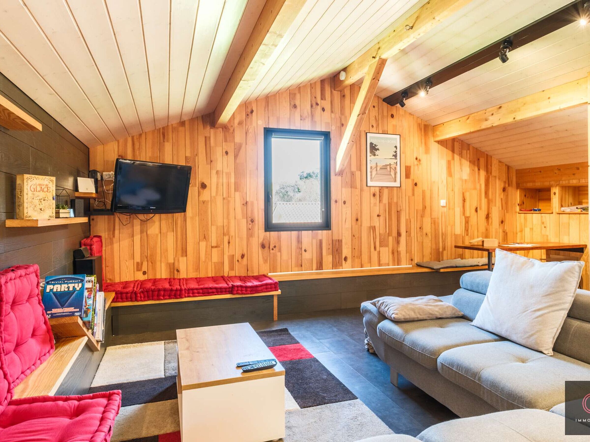 A cozy room with wooden walls, a flat-screen TV, a sofa, a red bench, and a small table.