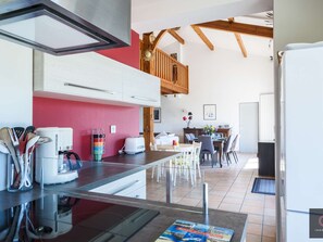 Eine moderne Küche mit roter Akzentwand, ein Essbereich mit Tisch und Stühlen sowie ein Schlafzimmer im oberen Bereich mit freiliegenden Holzbalken.