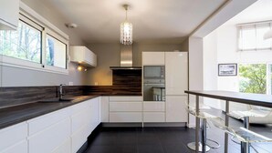 A modern kitchen with a dark countertop, white cabinetry, a built-in oven, and a hanging light fixture.