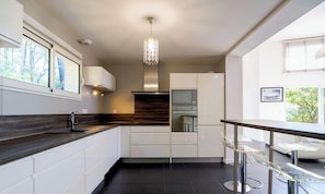A modern kitchen with a dark countertop, white cabinetry, a built-in oven, and a hanging light fixture. - Family villa with pool - 10 guests (Biscarrosse)