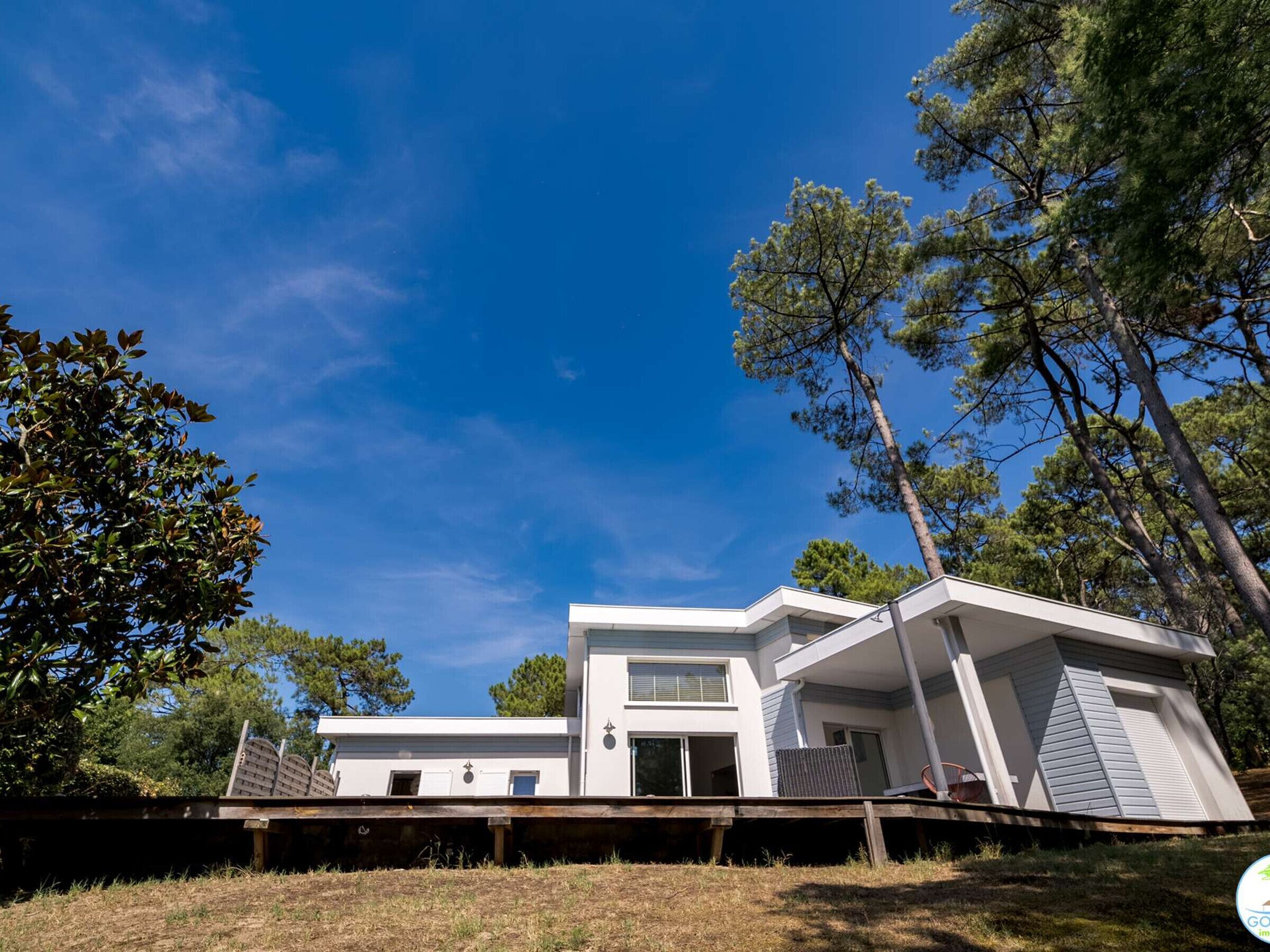 Een modern huis met twee verdiepingen, een plat dak, grote ramen en een terras.