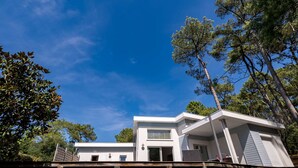 A modern two-story house with a flat roof, large windows, and a deck.