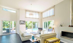 A spacious living area with a sofa, coffee table, and a fireplace. There are large windows and a view of the outdoors. - Family villa with pool - 10 guests (Biscarrosse)