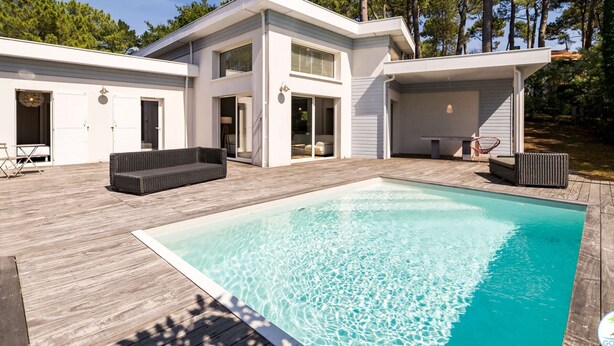 A modern two-story house with a swimming pool, outdoor furniture, and a deck.