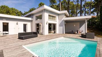 Een moderne, tweelaags woning met een zwembad, tuinmeubilair en een terras.