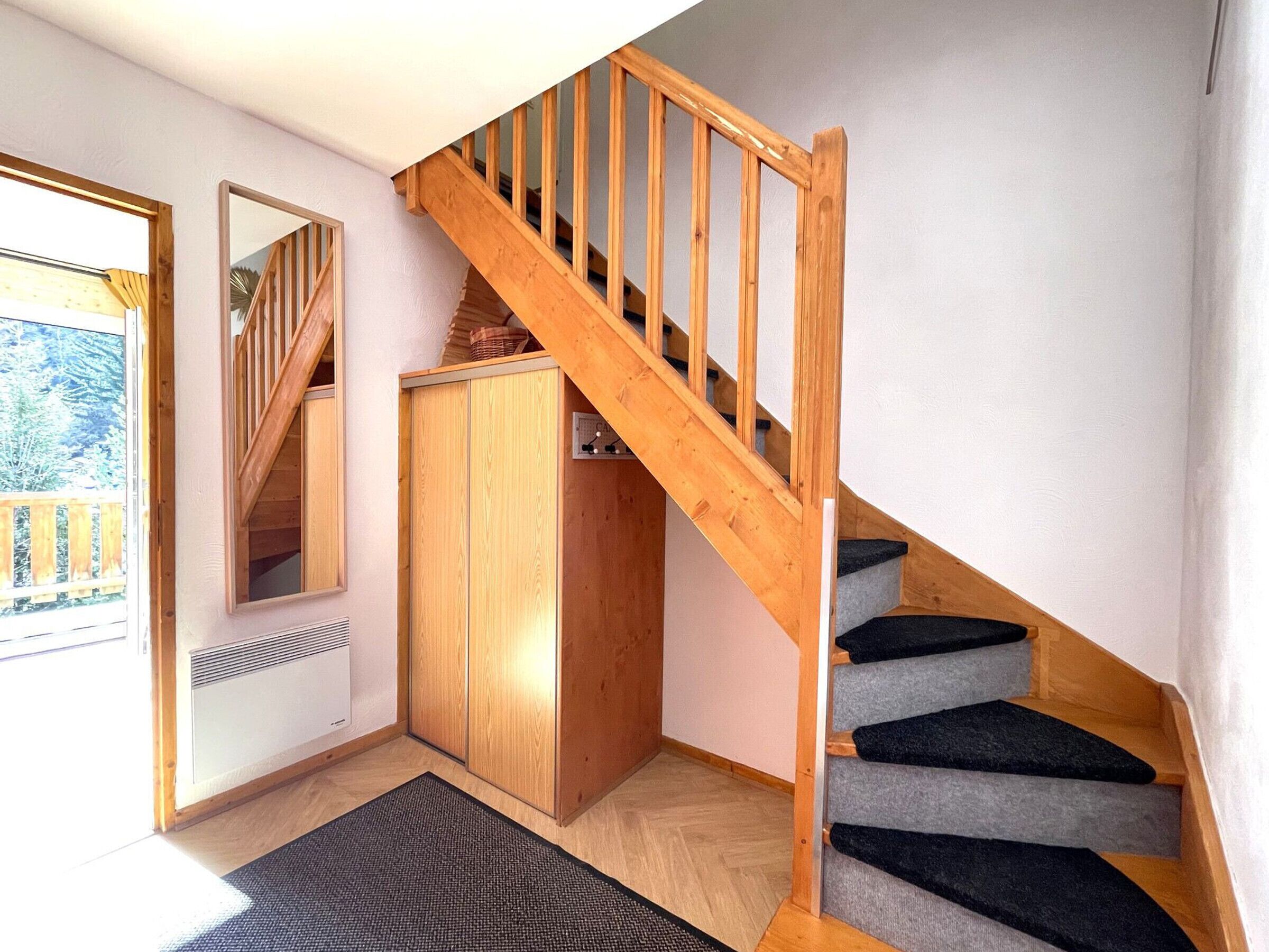 A wooden staircase with a handrail, a wooden wardrobe, and a mirror on the wall.