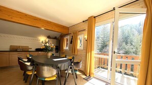 A dining area with a round table, chairs, and a view of a balcony with a wooden railing. - Comfortable duplex, slope view - 6 guests (Valfréjus)