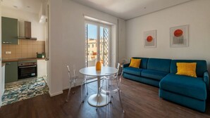 Ein modernes Wohnzimmer mit einem blauen Sofa, einem Esstisch mit Stühlen und einer Küchenzeile mit Herd und Schränken.