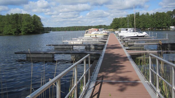 A wooden dock extending into calm water with boats docked, surrounded by trees.