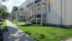 A multi-story building with balconies, a brick pathway, and a green lawn.