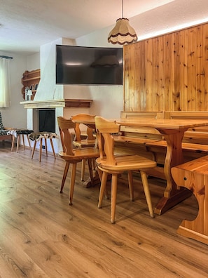 A wooden dining area with a TV mounted on the wall, wooden chairs, and a table. - Casa Castoro - Nel cuore della Val di Peio (Peio Fonti)