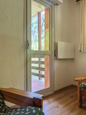 A room with a wooden floor, a white wall, a sliding glass door leading outside, and a small wooden table. - Casa Castoro - Nel cuore della Val di Peio (Peio Fonti)
