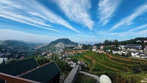 Vista panorámica de un pueblo con campos en terrazas, una colina destacada y cielo despejado.