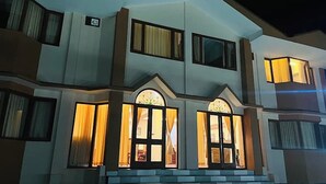 Un edificio de varios pisos con una entrada destacada, que incluye una escalera que lleva a una puerta con paneles de vidrio y cortinas.