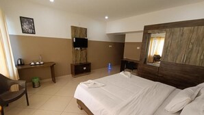 Habitación de hotel con cama, escritorio, silla, televisor y espejo.