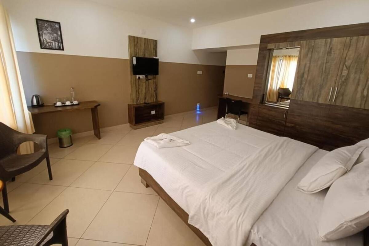 A hotel room with a bed, a desk, a chair, a TV, and a mirror.
