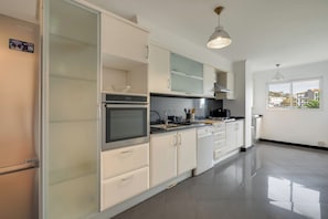 Une cuisine moderne avec des meubles blancs, un four encastré et une grande fenêtre donnant sur l’extérieur.
