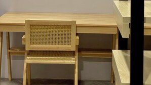 Un bureau en bois avec une chaise devant, une structure à ossature noire sur la droite et un mur uni en arrière-plan.