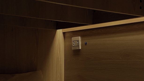 Un coin de pièce avec une tête de lit en bois, un lit et une prise de courant au mur.