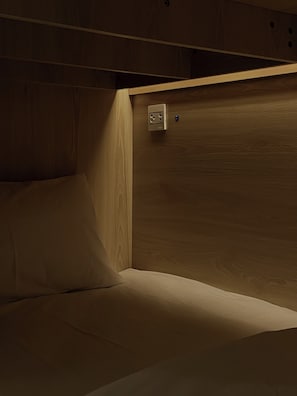 Un angolo di stanza con una testiera di legno, un letto e una presa elettrica.