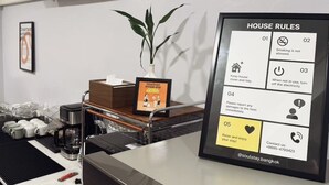 Un comptoir d’accueil d’hôtel avec un panneau encadré indiquant les règles de l’établissement, une plante en pot et un coin café.
