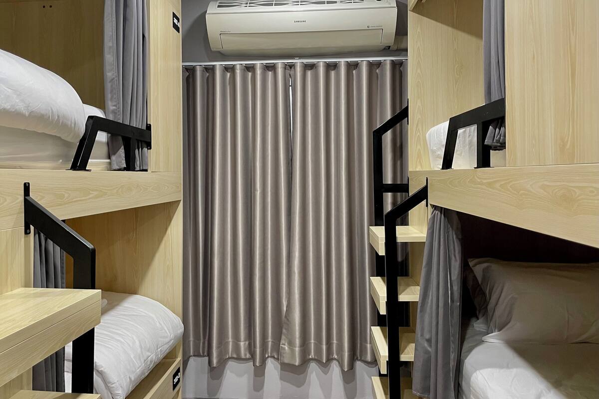 A bunk bed room with a ceiling-mounted air conditioner, a curtain, and a wooden floor.
