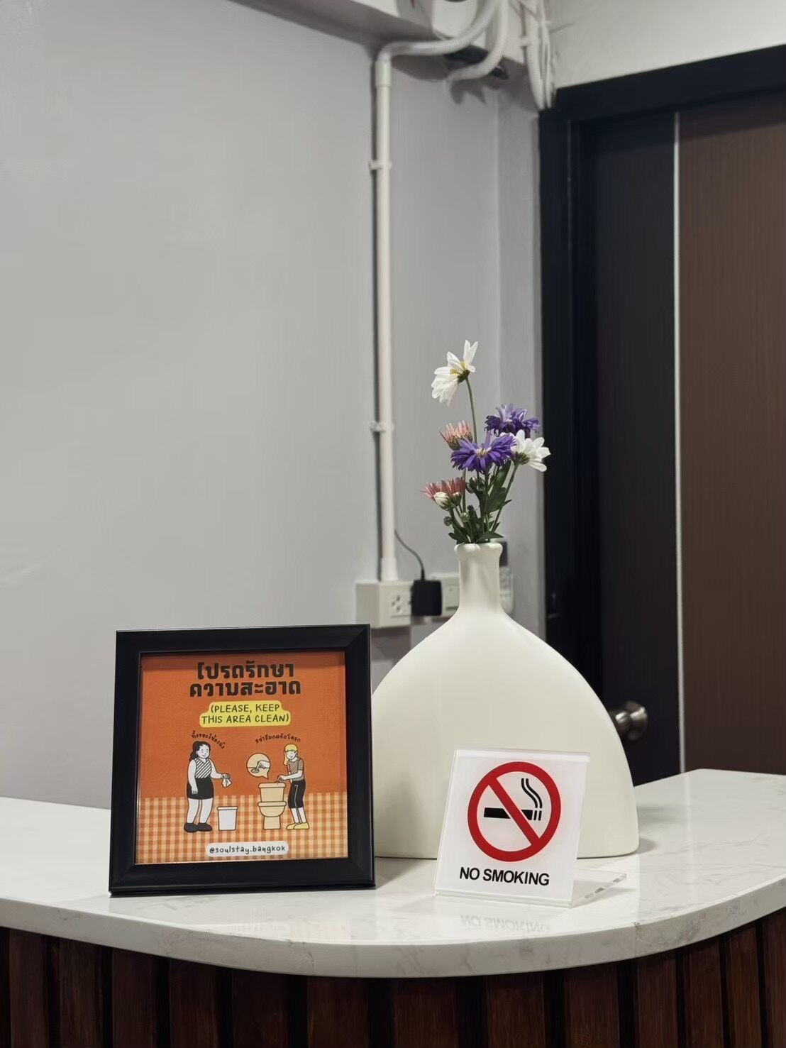 A framed sign with a toilet and a no-smoking sign on a counter.