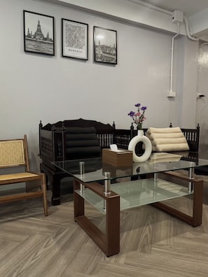 Un soggiorno moderno con un tavolino in vetro, un divano nero, una poltrona in rattan e un vaso con fiori.