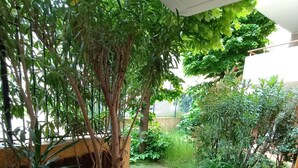 A patio with a white table and chair, surrounded by lush greenery and a tiled floor. - Charming apartment for 4 people with a terrace and air conditioning (Grasse)