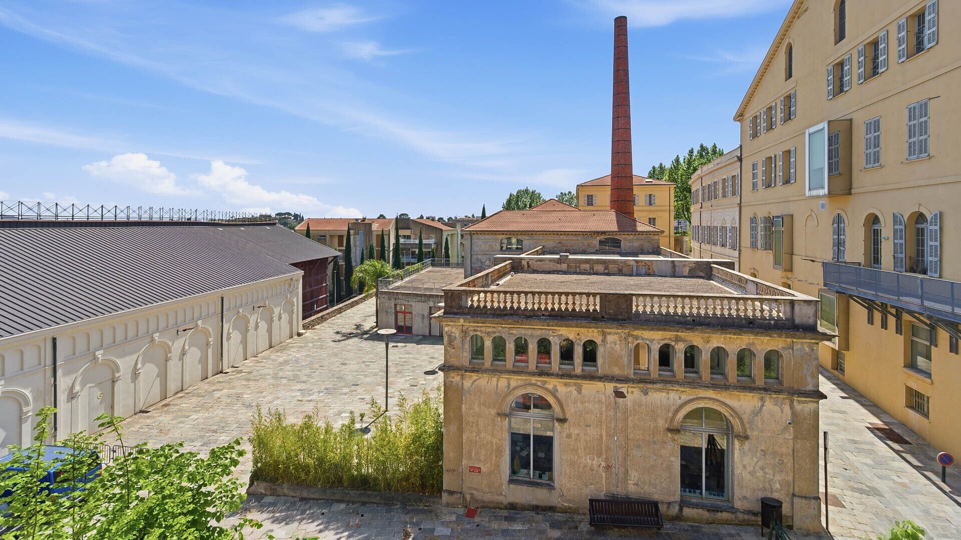 A courtyard with a building featuring arched windows and a central chimney.
